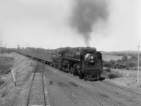 A Canadian National Railways passenger train, hauled by steam locomotive no. 6211, pulls toward a railway station