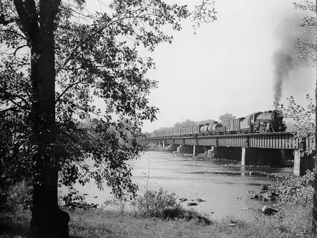 A steam locomotive hauls a freight train across Vaudreuil Bridge