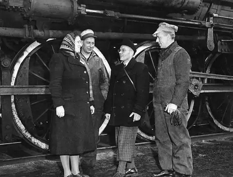 Railway workers chat with immigrants beside a locomotive