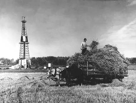 A farmer harvests hay near Imperial Oil drilling rig no. 1