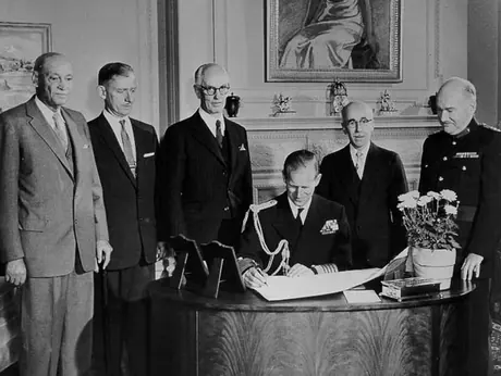 Prince Philip signs documents in the presents of embassy officials during the 1957 Royal visit to Ottawa with Queen Elizabeth