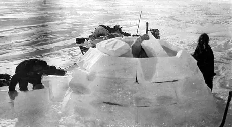 Three Inuit men building an igloo, with dogsled in the background.
Original caption: