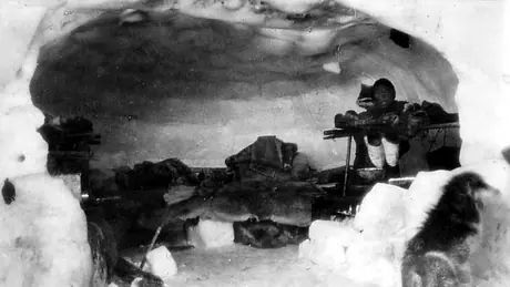 Inuk child inside an igloo, with caribou skins covering the sleeping platform.
Original caption: