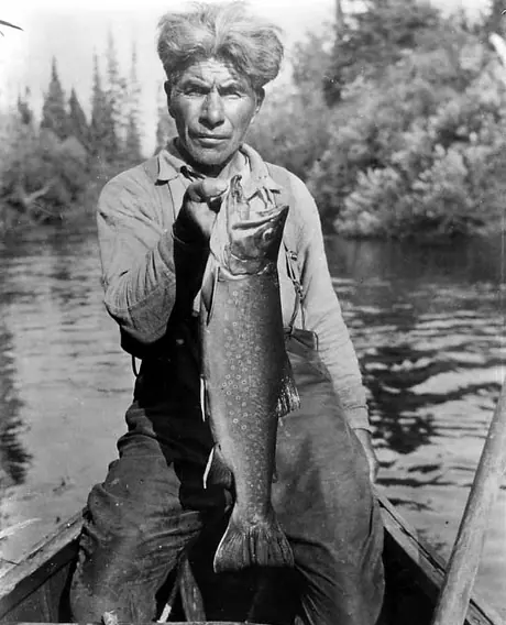 Cree fisherman in canoe holding large speckled trout.
Original caption: