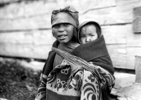 Girl with baby strapped to her back, both inside a decorative blanket shawl