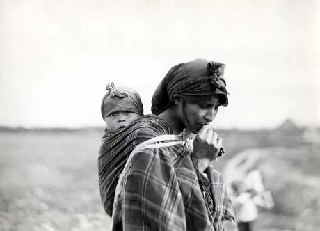 Woman in plaid shawl, carrying baby strapped to her back