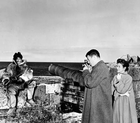 Tourists photographing young Inuk in traditional hide clothing along shore at Ft. Prince of Wales