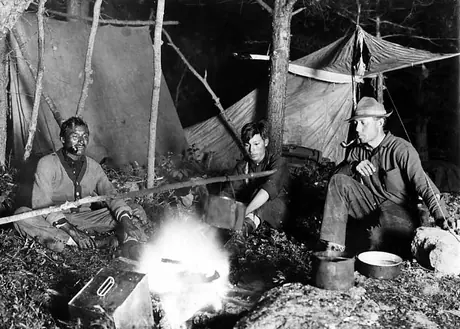 Two Ojibwa men with camp companion cooking at night by campfire.
Original caption: