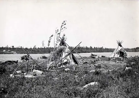 Two Ojibwa birch bark conical wigwams and two birch bark canoes on lakeshore.
Original caption: