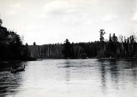 Ojibwa man paddling across a lake in a birch bark canoe.
Original caption: