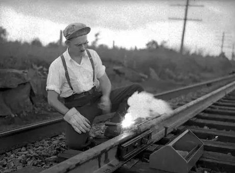 Bonding a new rail line.  A signal department employee connects rails by a short length of steel to ensure good electrical contact for train detection.
