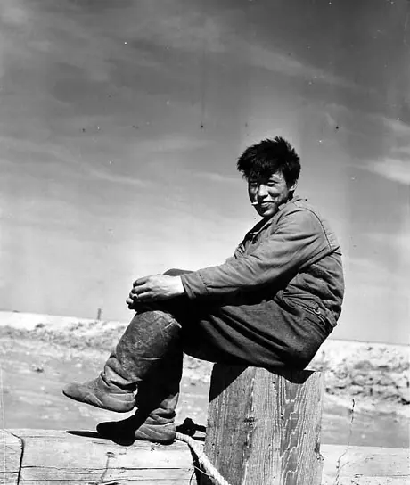 Young Inuk in skin mukluks, seated on fence post
