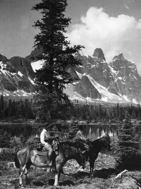 A pair of riders by Moat Lake, with Mts. Turret, Geikie, and Barbican Peaks in the distance