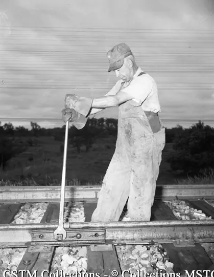 Angle bars in place, the bolts holding them are tightened wait a long-handled track wrench by section man, H. Baker of Ernestown