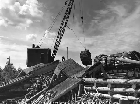 Bundles of wood being lifted from rail cars into the water