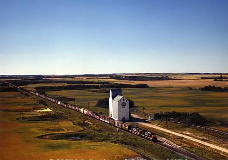 Freight train passing a grain elevator with a crib annex at Smart, Manitoba