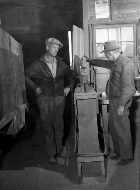The elevator agent weighs in a truck with grain on the floor scale inside the elevator.  The farmer looks on.