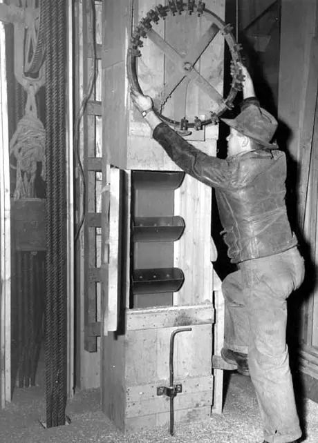 The elevator agent's assistant sets a wheel indicating the bin to which grain will be elevated by the scoop belt visible below the wheel