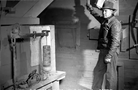 Elevator agent loading a box car.  The handle in his right hand controls the flow of grain into the car.  The scale is preset and he watches to see when the set weight is loaded