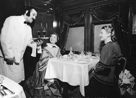 A waiter serves wine to two passengers in the dining car of the Museum Train